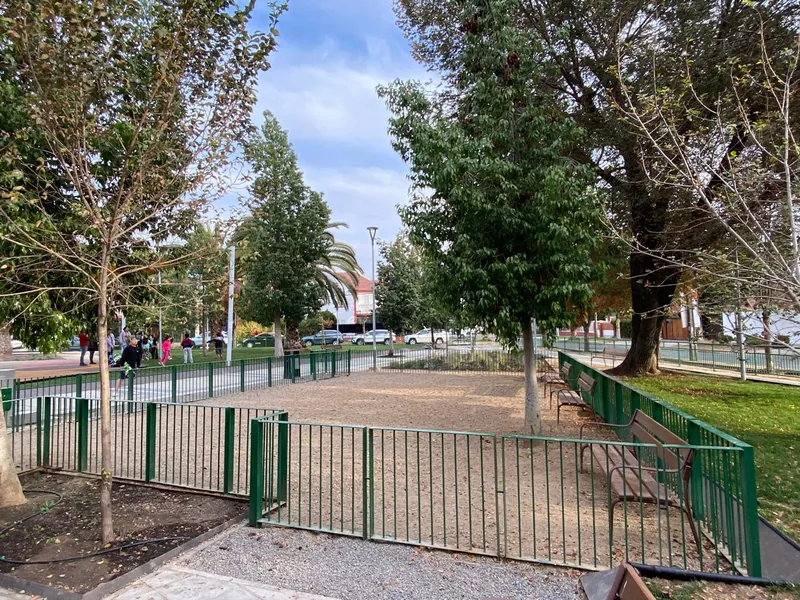 Zona de mascotas cercada, con árboles y bancas, en la Plaza Gabriela Mistral